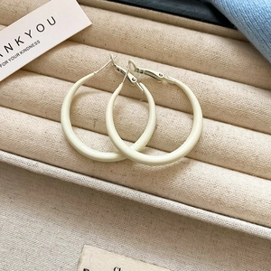 Close-up of cream white enamel hoop earrings on a beige linen jewelry display box