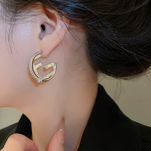 Macro shot of gold-plated 18K F-shaped stud earring with paved white zircons on ear