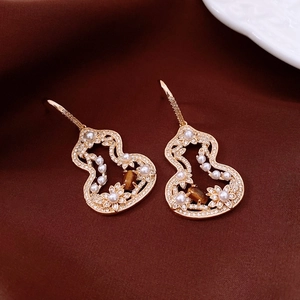 Close-up of gold hollow gourd earrings with tiger eye stones and pearls on fabric