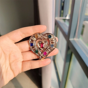 Close-up of golden heart brooch with colorful rectangle crystals and red center stone
