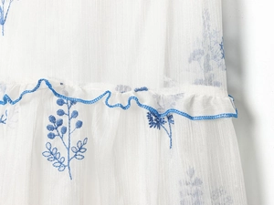 Detail aus weißem Chiffon mit blauer Blumenstickerei und gerüschtem Saumfinish