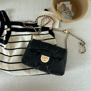 Detail of black quilted leather shoulder bag with gold chain strap and metal buckle