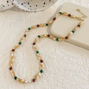 Detail of bohemian necklace with yellow shell beads, red stones, and white freshwater pearl