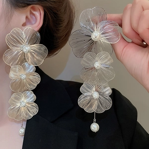 Dettaglio di grandi orecchini a fiore dorati con perle bianche e trama di petali fini