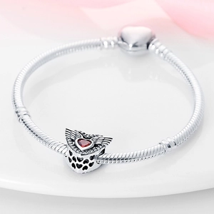 Detailed macro view of a silver heart charm with red gem and wings on a beaded bracelet