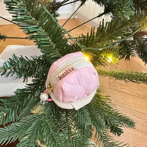 Pink quilted round earphone case with pearl pendant hanging on a festive tree branch