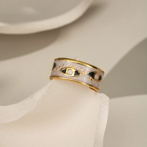 Detail of gold enamel evil eye ring on white stone texture background with high-end finish
