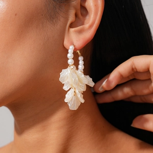 Elegant bohemian drop earrings with white pearls and resin petals on a female model