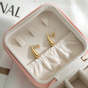 Detailed close-up of polished gold teardrop earrings inside a pink leather jewelry box