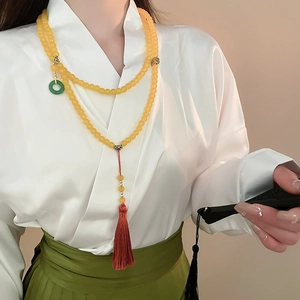 Gros plan sur un long collier de perles avec pendentif jade vert et pompons en soie rouge