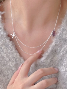 Close-up of layered silver swallow necklace with purple teardrop gemstone on a sweater