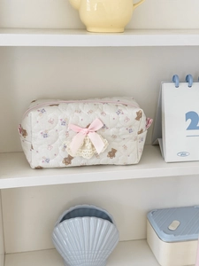 Detail of white quilted bear pouch featuring heart texture and pink bow accents