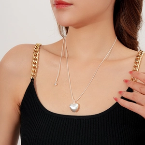 Gros plan d'un collier avec pendentif cœur argenté brossé porté sur une chaîne serpent chic