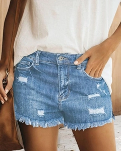 Detail of high-waisted blue denim shorts with distressed ripped holes and frayed hems