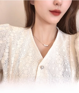 Close-up of minimalist gold necklace with three pearls on elegant lace clothing