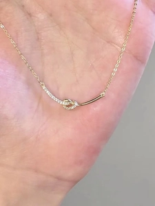 Detailed view of a gold S925 sterling silver bow knot pendant with diamonds held in hand