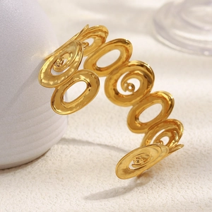 Macro d'un bracelet spirale en acier inoxydable doré sur un support texturé beige