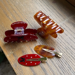 Detailed set of acetate hair clips including deep red and amber claw clips on a wooden surface