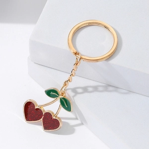 Cute golden heart cherry keychain with red glitter details on a white geometric block