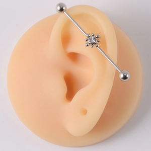 Silver industrial barbell earring with crystal flower design on a silicone ear model