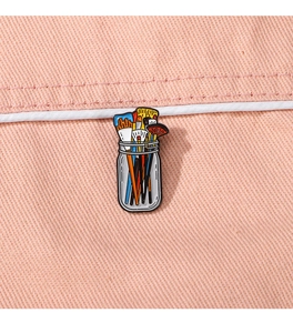 Detail of colorful paintbrush enamel pin on pink fabric background for artists
