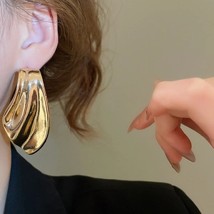 Macro detail of large gold wave earrings with liquid metal texture on a model