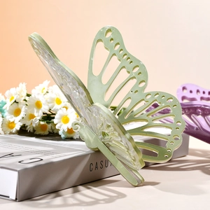 Hellgrüne Schmetterlings-Haarklammer mit filigranen hohlen Flügeln vor Blumenhintergrund