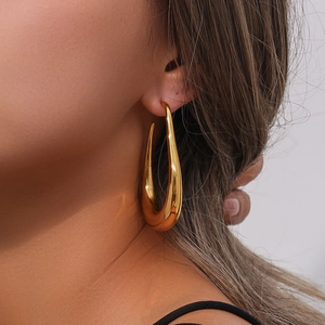 Side view of large hollow curved gold earrings showing polished texture on model