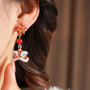 Detail of lion dance earring featuring red floral studs and soft white plush texture