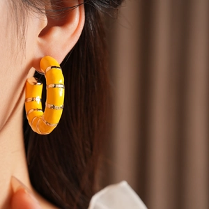 Close-up of vintage yellow enamel C-shaped earrings with gold trim worn by a model