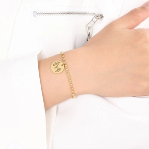 Detailed view of gold beaded chain bracelet with a cutout family pendant on a model