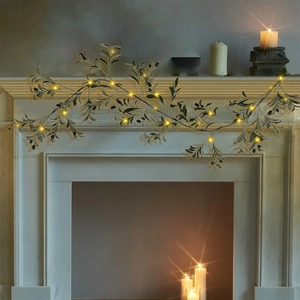 Detail of faux olive wreath with warm LED lights and black fruits on a white fireplace