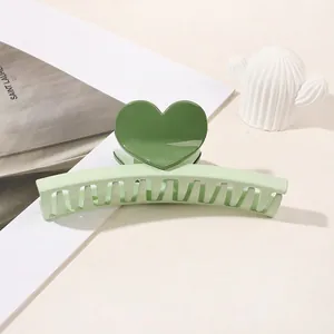 Close-up of a two-tone green heart hair claw clip on a minimalist white desk setting