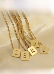 Macro detail of polished 18K gold plated stainless steel square initial letter pendants