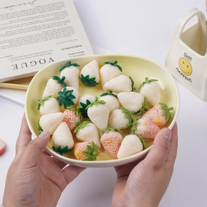 Realistic PVC strawberry models in white and pink displayed in a ceramic dish
