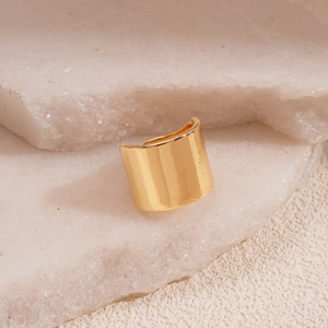 Detailed close-up of wide polished gold ring on white textured stone display