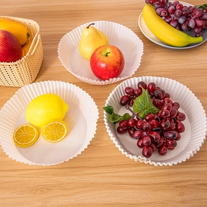 Three disposable round air fryer paper liners shown with fresh fruit on a wooden table