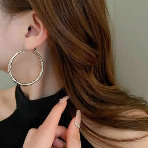 Macro detail of large silver striped hoop earrings on model with ripple texture effect