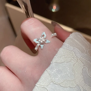Détail d'une bague papillon en argent avec émail bleu clair et perles sur de la dentelle