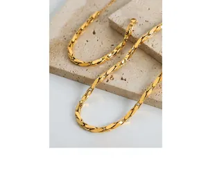 Detail shot of flat olive-shaped interlocking gold-plated chain on beige stone