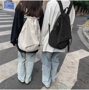 Street style view of white and black washed canvas backpacks worn by two people outdoors