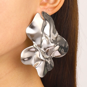Detailed close-up of large irregular silver earrings with a fluid wrinkled texture