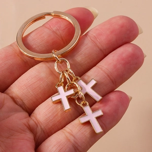 Close-up of hand holding a golden keychain with three pink enamel cross pendants