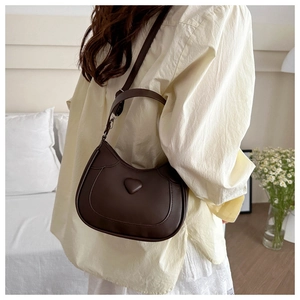 Detail of a dark brown crescent shoulder bag with heart accent and adjustable strap