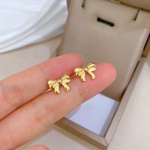 Minimalist gold bow earrings in titanium steel held by hand for a delicate look