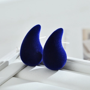 Detail view of dark blue velvet teardrop earrings placed on a white leather jewelry box