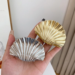 Polished gold and silver shell hair claws held by a hand showing size and texture