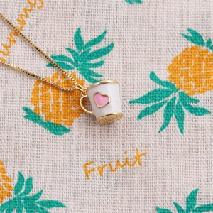 Gold chain necklace with white cup pendant and pink heart on a patterned fabric