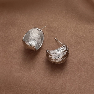Macro view of C-shaped hammered silver earrings on dark brown silk fabric