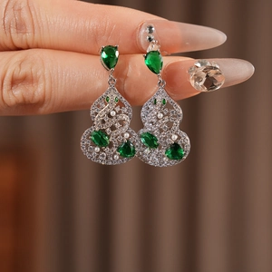 Detailed close-up of a silver gourd earring set with green stones and pearls on a model